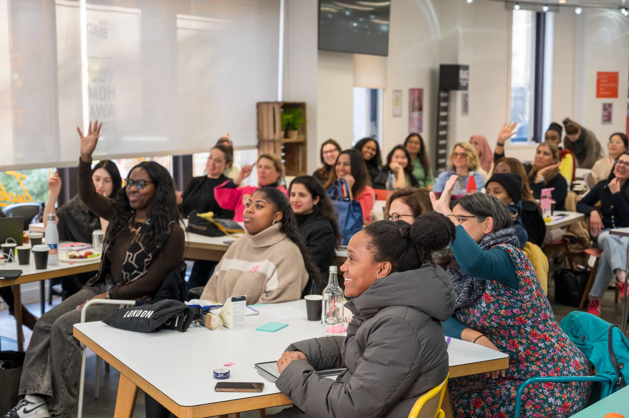 Women at desks with their hands up.