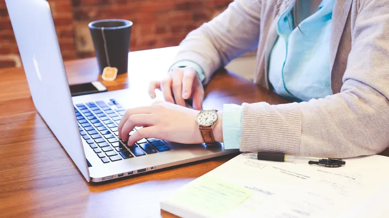 A student working on their laptop next to a notebook and a cup